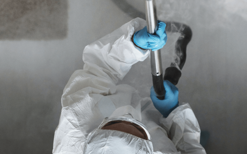 IEA Medical - Person in einem weißen Ganzkörper-Overall und blauen Handschuhen hat einen Desinfektionsstab in der Hand