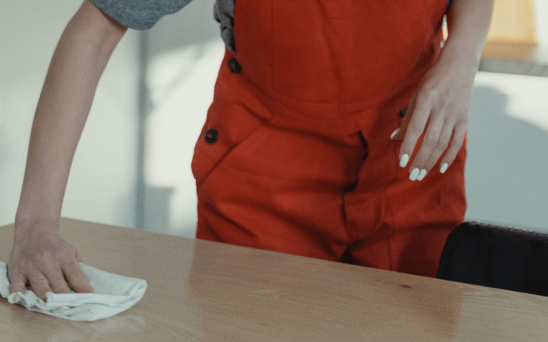 IEA Medical - Person in roter Latzhose wischt mit einem Tuch über einen Holztisch